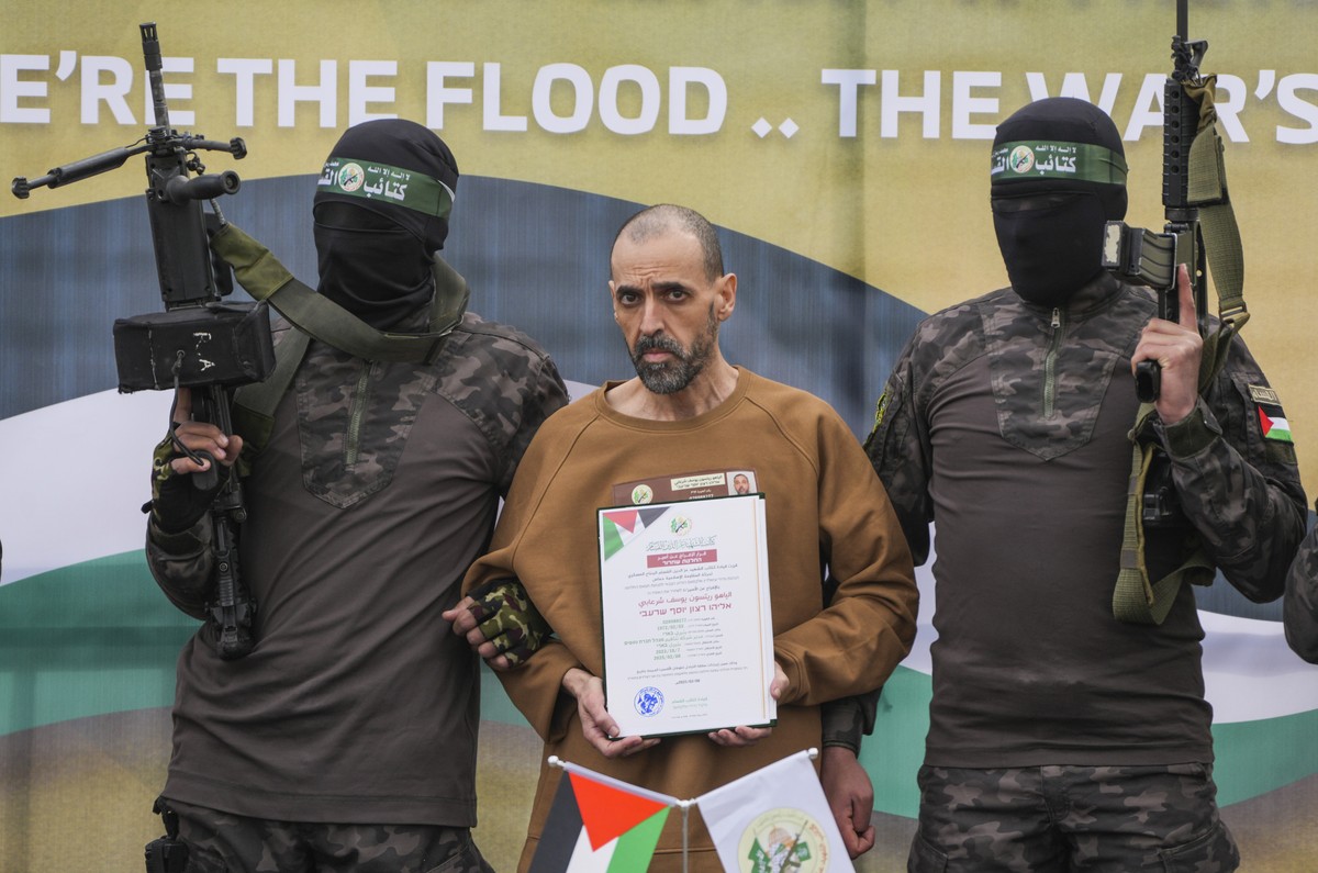 Israeli captive, Eli Sharabi, who has been held hostage by Hamas in Gaza since October 7, 2023, stands on a stage escorted by Hamas fighters before being handed over to the Red Cross in Deir al-Balah, ...