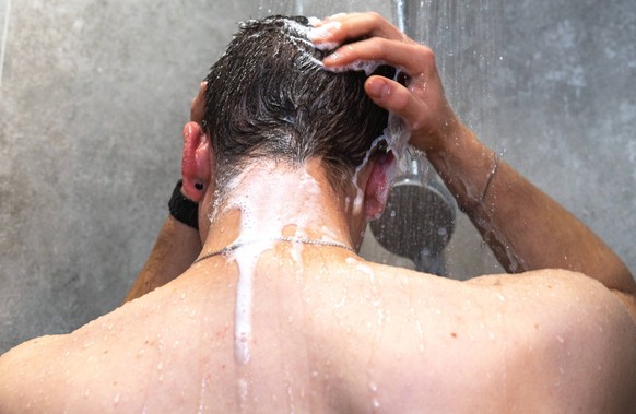 Bavaria, Germany - November 26, 2023: A young man stands under the shower and washes himself with warm running water *** Ein junger Mann steht unter der Dusche und wäscht sich mit warmen fließendem Wa ...