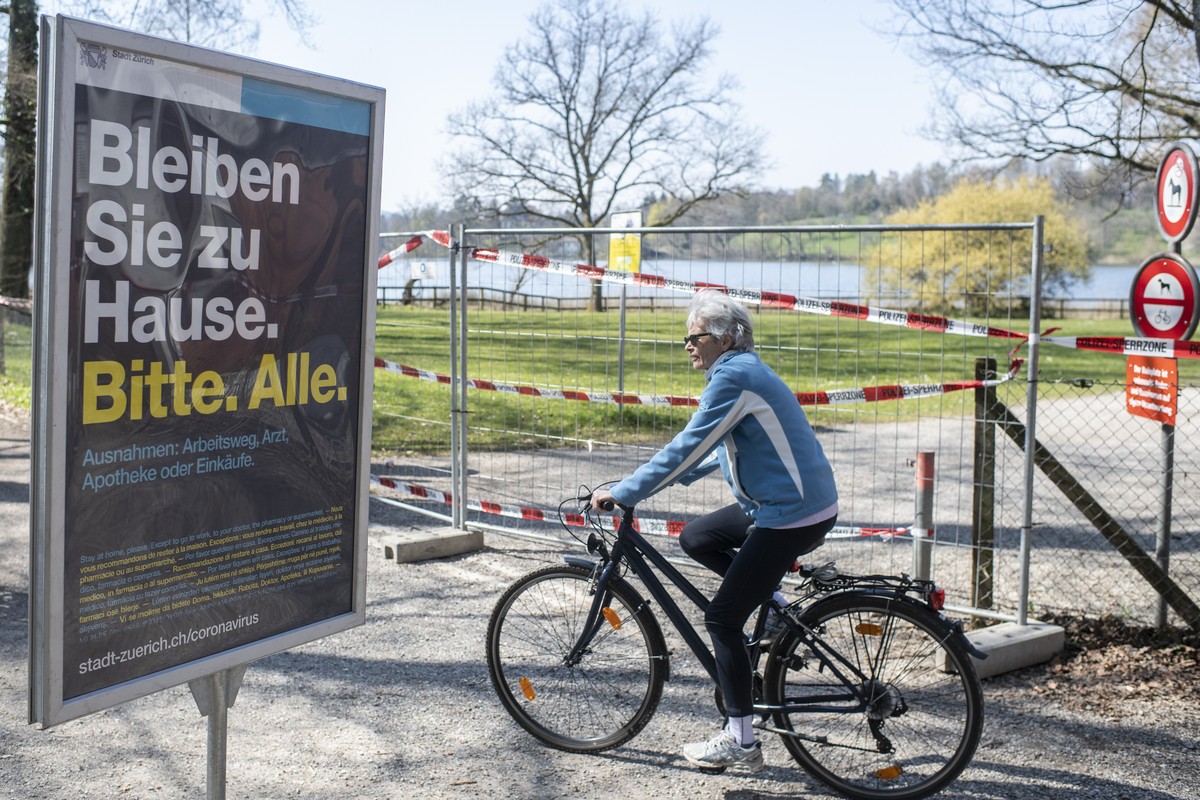 Eine Frau faehrt auf ihrem Rad neben einem Plakat "Bleiben Sie zu Hause. Bitte. Alle." um den abgesperrten Bereich am Katzensee, aufgenommen am Freitag, 3. April 2020 in Zuerich.(KEYSTONE/En ...