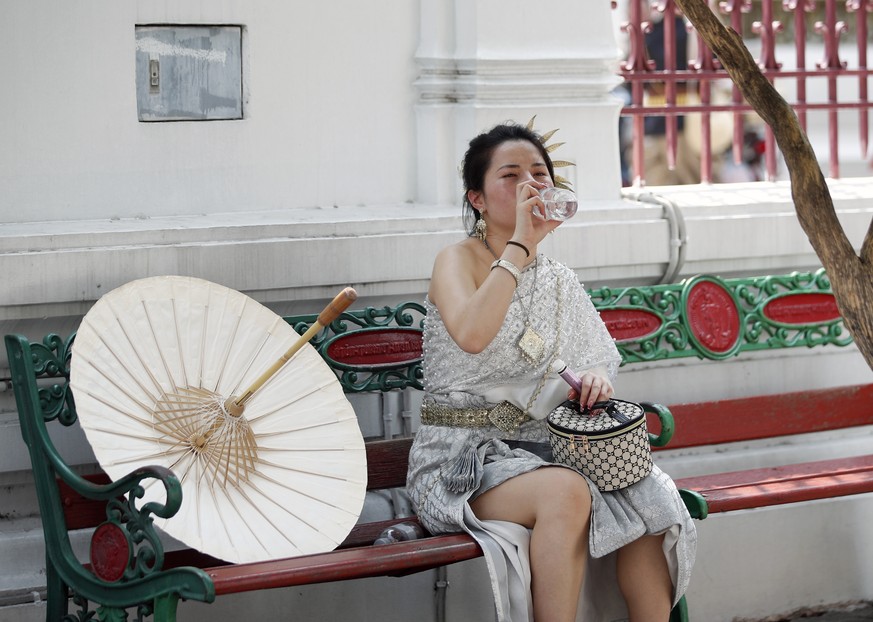 epa11321379 A Chinese tourist dressed in Thai traditional rented costume drinks water during hot weather at the Temple of Dawn or Wat Arun in Bangkok, Thailand, 06 May 2024. Thailand is facing a sever ...