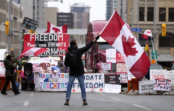 A protester waves a Canadian flag in front of parked vehicles on Rideau Street at a protest against COVID-19 measures that has grown into a broader anti-government protest, in Ottawa, Ontario, Friday, Feb. 11, 2022. (Justin Tang/The Canadian Press via AP)