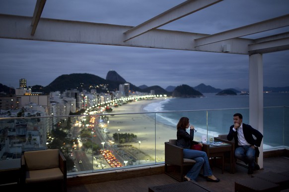 FILE - In this Aug. 16, 2013 file photo, tourists sit in a bar at a hotel overlooking Copacabana beach, in Rio de Janeiro, Brazil. Hundreds of thousands of foreign visitors are expected for the Olympi ...