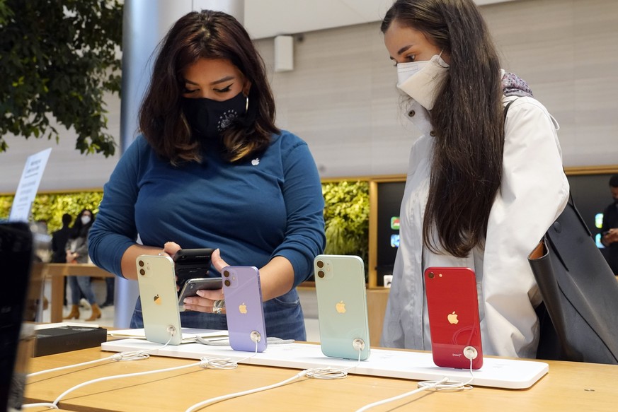 An Apple store employee, left, assists a customer with an iPhone 13 on its first day of sale, in New York, Friday, Sept. 24, 2021. (AP Photo/Richard Drew)