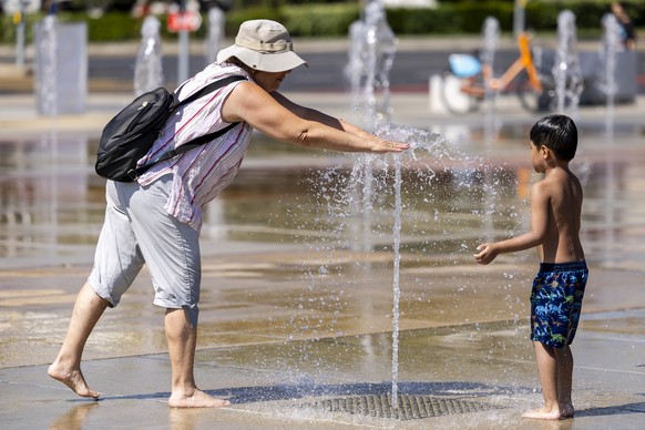 A woman and a kid off cool off in a water-jet fountain on the Place des Nations, during a heatwave alert, in Geneva, Switzerland, Wednesday, July 2, 2025. (KEYSTONE/Salvatore Di Nolfi)