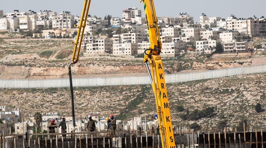 epa05865828 Worker stand at the construction site of the Israeli settlement of Neve Ya&#039;akov north of Jerusalem, and the West Bank town of al-Ram with the separation barrier in the background, 23  ...