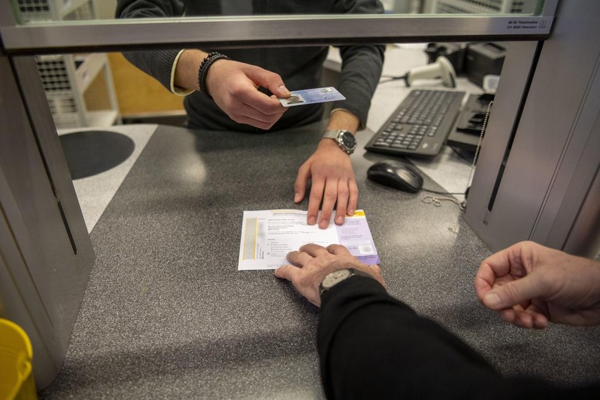 [Gestellte Aufnahme] Um ein Paket abzuholen, haendigt ein Kunde am Schalter der Post-Filiale Sihlfeld den Abholschein und seine Identitaetskarte einem Postmitarbeiter aus, welche dieser prueft, fotogr ...