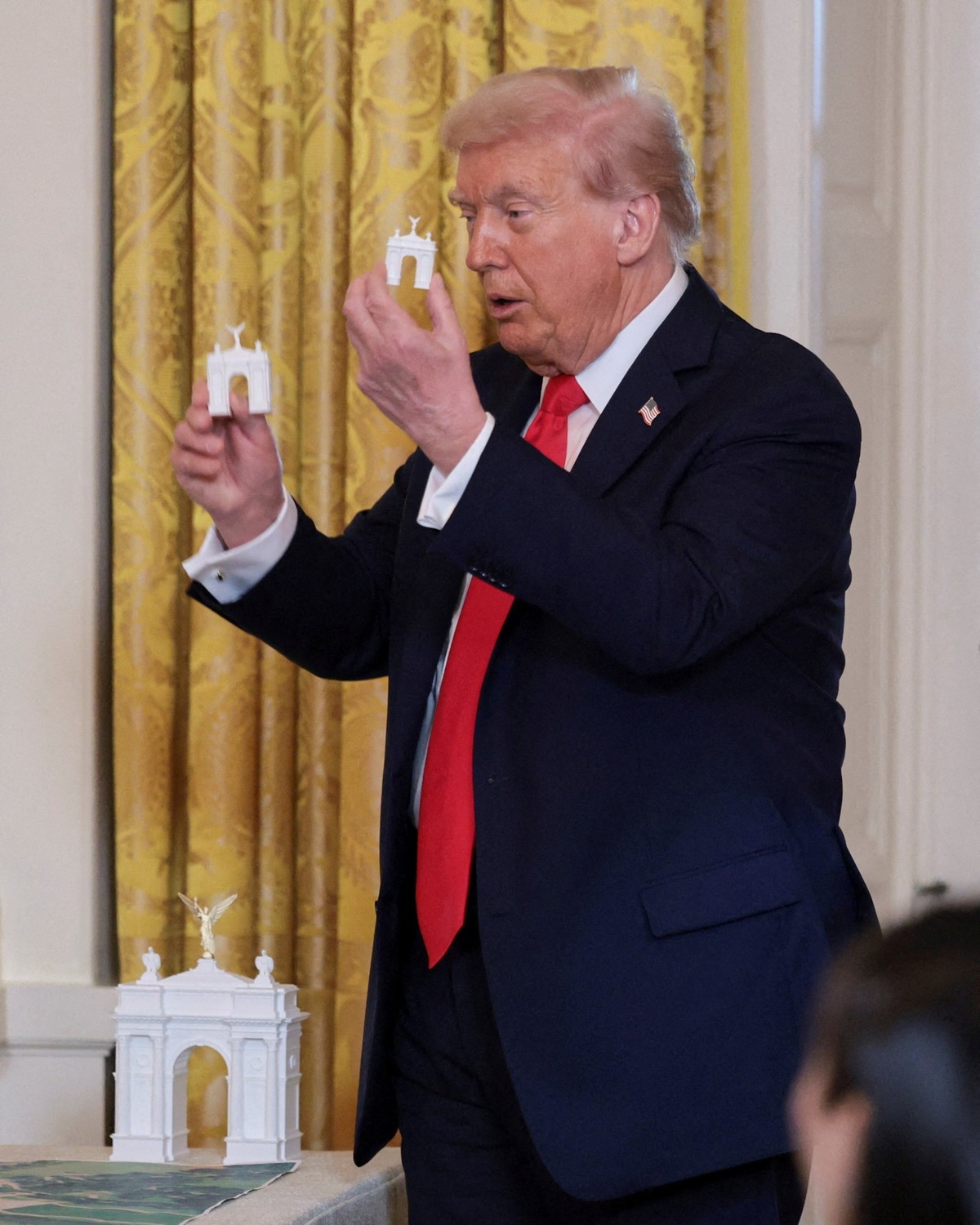 U.S. President Donald Trump holds models of an arch monument during a ballroom dinner in the East Room at the White House in Washington, D.C., U.S., October 15, 2025. REUTERS/Jonathan Ernst