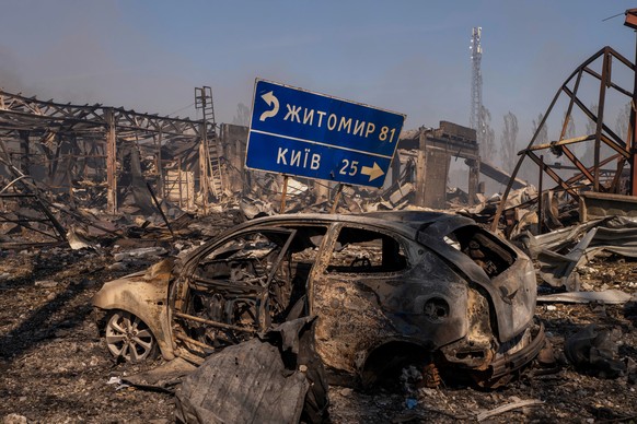A view of a destroyed car stands amid damaged buildings, with a road sign showing the direction and distance to Kyiv and Zhytomyr after a Russian attack struck a warehouse, followed by an explosion, i ...
