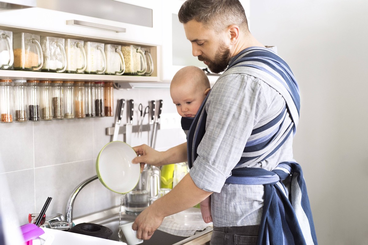 Father with baby son in sling at home doing the dishes model released Symbolfoto property released PUBLICATIONxINxGERxSUIxAUTxHUNxONLY HAPF01420