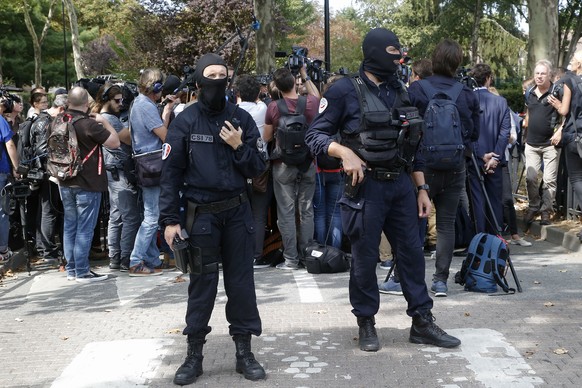 Hooded police officers watch out while French Interior Minister Gerard Collomb answers reporters after a knife attack Thursday, Aug. 23, 2018 in Trappes, west of Paris. A man flagged by French authori ...