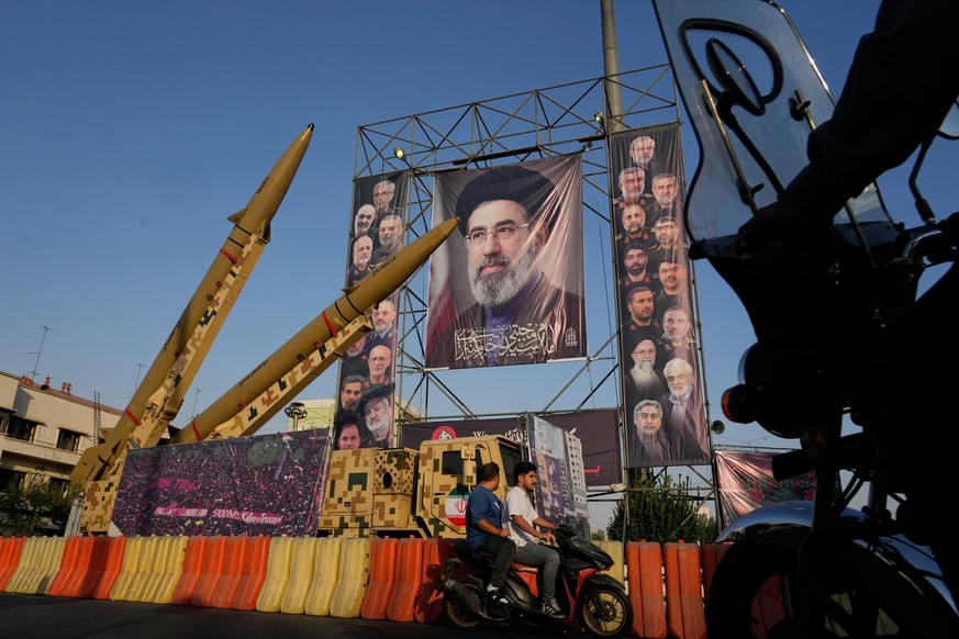 Motorbikes drive past Iranian missiles and banners showing portraits of the Iranian Supreme Leader Ayatollah Mojtaba Khamenei, center, and the late armed forces commanders and nuclear scientists, who  ...