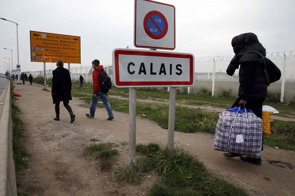 A migrant carries bags with his belongings as he walks past the Calais city limit sign on the eve of the evacuation and transfer of migrants to reception centers in France, and the dismantlement of th ...