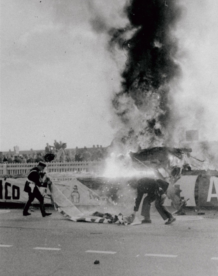 French police use a banner torn from the barrier in the background to beat out the flames on the body which observers said they believed was the body of French driver Pierre Levegh. The Mercedes, driv ...