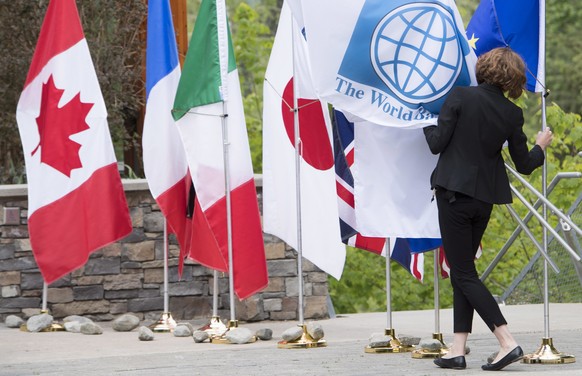 A staffer tries to secure the flags blowing in the wind during a meeting for the G7 Finance and Central Bank Governors in Whistler, British Columbia, Thursday, May 31, 2018. (Jonathan Hayward/The Cana ...