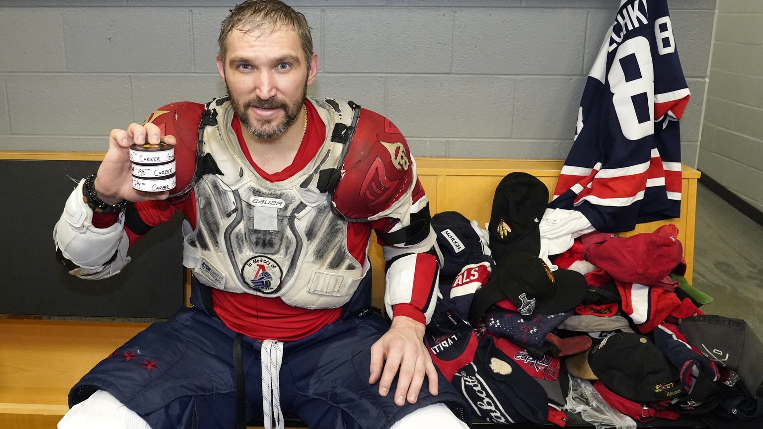 Washington Capitals&#039; Alex Ovechkin holds his 798, 799, and 800th career goal pucks in the locker room next to hats collected for his hat trick after an NHL hockey game against the Chicago Blackha ...