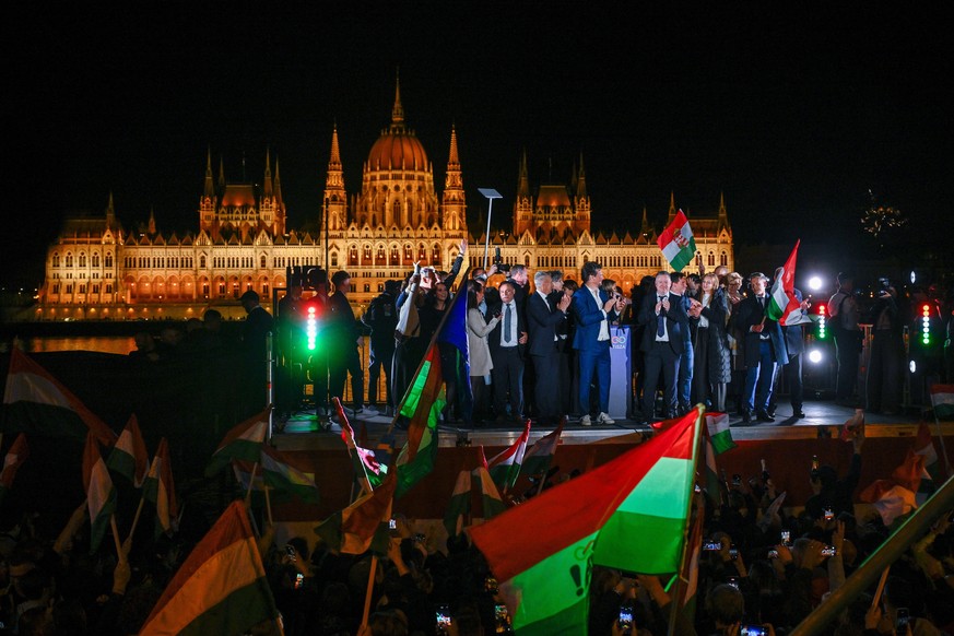 epa12886201 Chairman of the opposition Tisza Party Peter Magyar (R) holds a national flag as he celebrates with supporters after his party won landslide victory in the general elections in Budapest, H ...