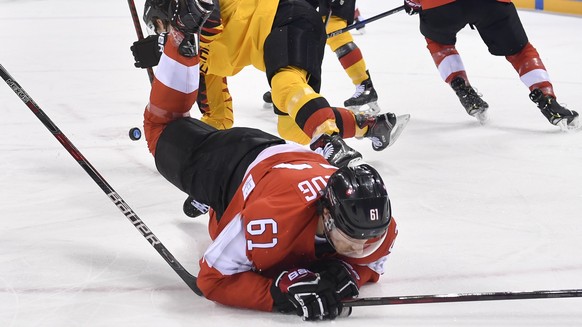 Fabrice Herzog of Switzerland, right, trips over Patrick Hager of Germany stick, left, during the men ice hockey play-off qualification match between Switzerland and Germany in the Kwandong Hockey Cen ...
