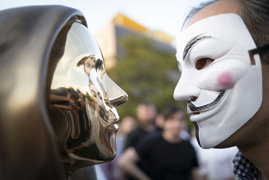 A man wearing a a Guy Fawkes mask looks at a newly unveiled statue of the mysterious developer of the Bitcoin digital currency in Budapest, Hungary, Thursday, Sept. 16, 2021. A bronze statue was unvei ...