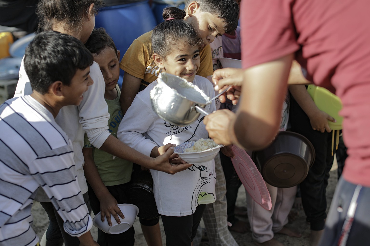 epa10938583 Palestinian children receive food between tents set up for Palestinians seeking refuge on the grounds of a United Nations Relief and Works Agency for Palestine Refugees (UNRWA) center in K ...