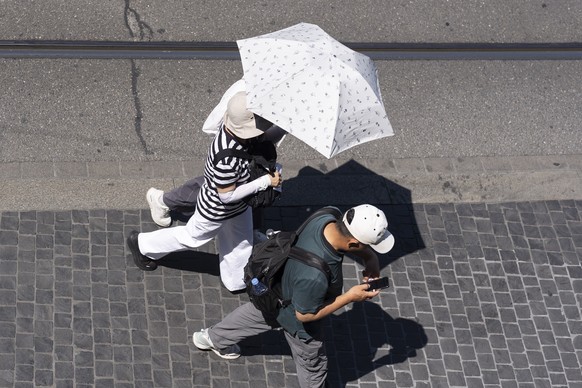 Menschen laufen mit Sonnenhut, Sonnenschirm und Armlingen auf dem Limmatquai, fotografiert am Freitag, 19. Juni 2026 in Zuerich. Seit Donnerstag gibt der Bund Hitzewarnungen der Stufen 3 und 4 heraus. ...