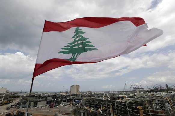 A Lebanese flag set by citizens flies in front the site of Tuesday&#039;s explosion that hit the seaport of Beirut, Lebanon, Sunday, Aug. 9, 2020. Lebanon&#039;s information minister resigned on Sunda ...