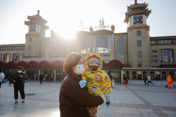 epa10397596 A woman wearing a face mask holds a child in front of Beijing Railway Station in Beijing, China, January 10, 2023. Chinese passengers travel domestically as the most im...