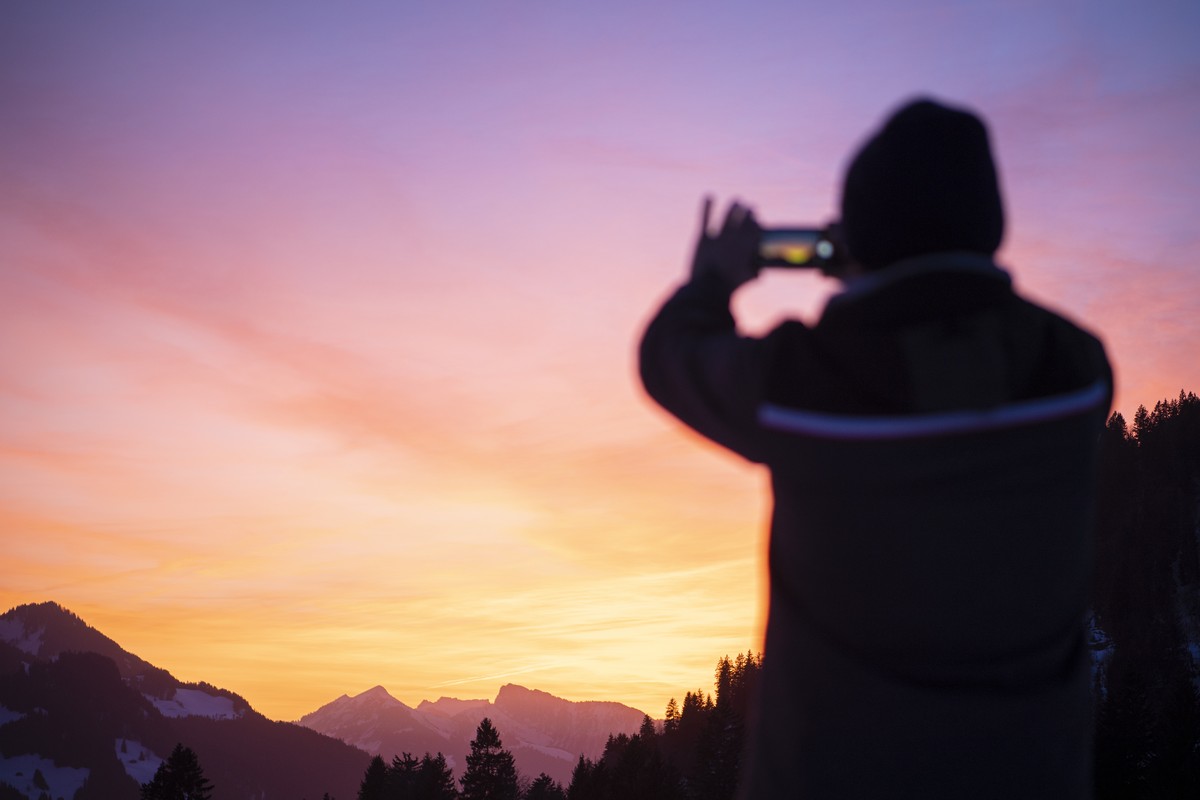 A man takes a picture with a smartphone of sunset next to the latest installation called "Mirage Gstaad" by American artist Doug Aitken, Wednesday, February 20, 2019, at Gstaad, Switzerland. ...