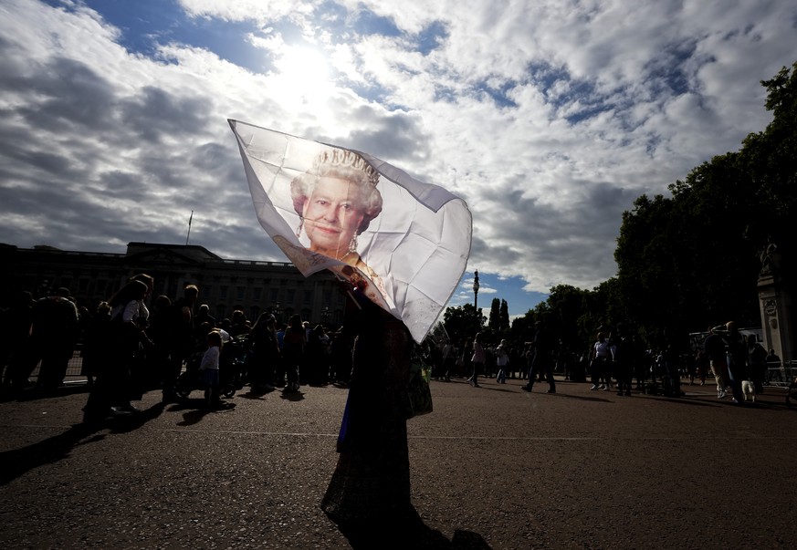 A flag is waved with an image of the late Queen Elizabeth II as thousands of people mourn and pay their respects at the gates of Buckingham Palace in London, Saturday, Sept. 10, 2022. (Nathan Denette/ ...