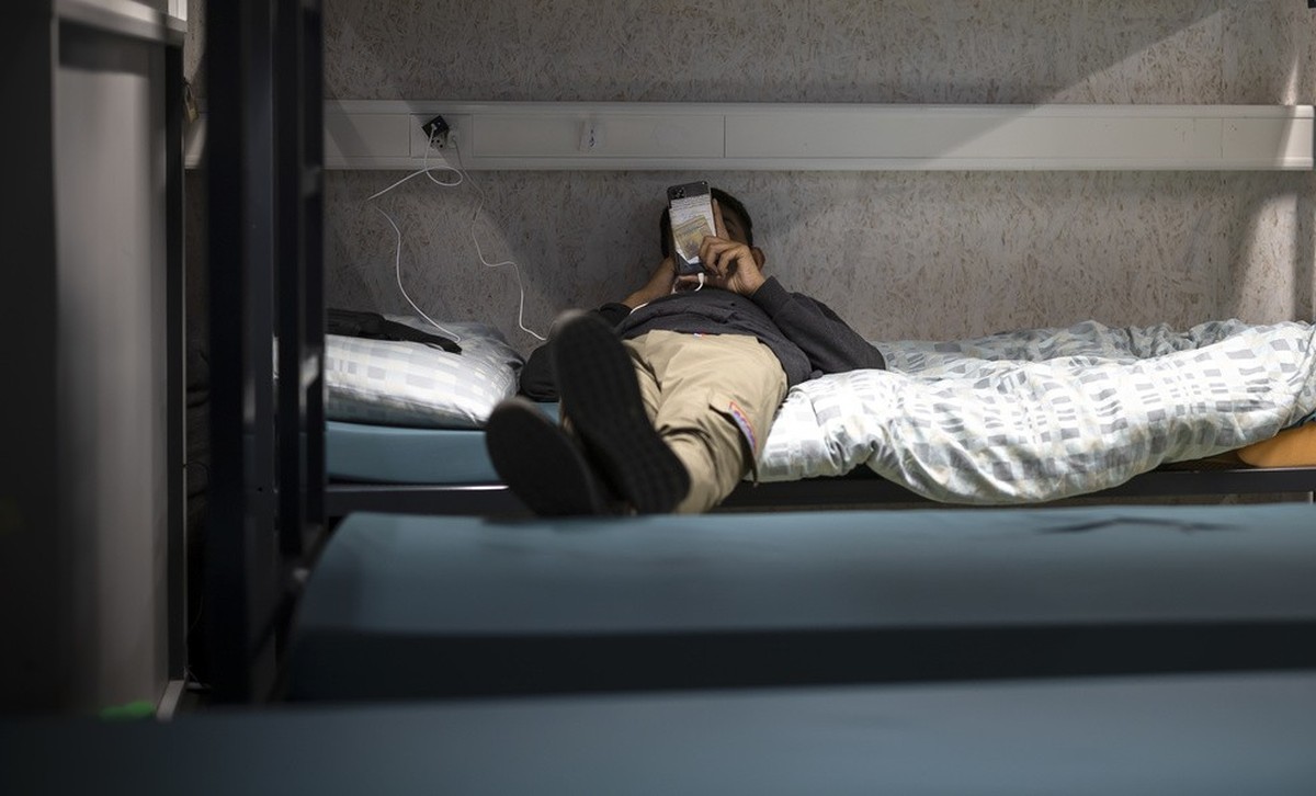 Ein Mann benutzt sein Mobiltelefon waehrend er in einem Schlafsaal auf einem Bett liegt, aufgenommen waehrend eines Medienrundgans im Bundesasylzentrum Zuerich, am Donnerstag, 27. Oktober 2022 in Zuer ...