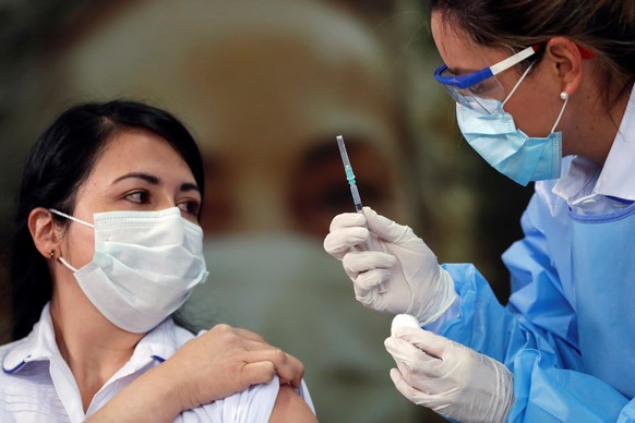 epa09021108 Health worker Claudia Benavides receives her first dose of the Pfizer-BioNTech vaccine at Clinica Colombia, in Bogota, Colombia, on 18 February 2021. Colombia on 17 February 2021 has begun ...