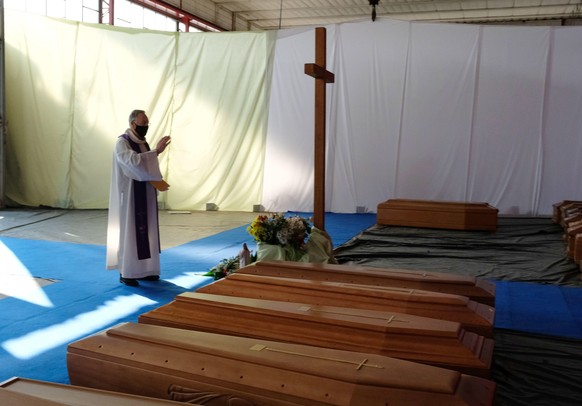 epaselect epa08340876 A priest wearing a protective face mask blesses the coffins of people who died of coronavirus, before they are taken away to the crematory ovens in other Italian regions with mil ...