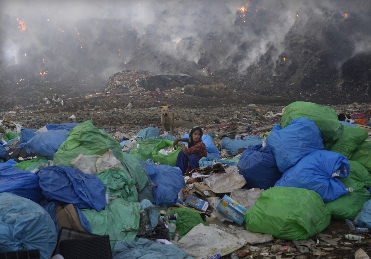 A ragpicker woman segregates items sitting at the edge during a fire at the Bhalswa landfill in New Delhi, India, Wednesday, April 27, 2022. India's capital, which like the rest of South Asia is  ...