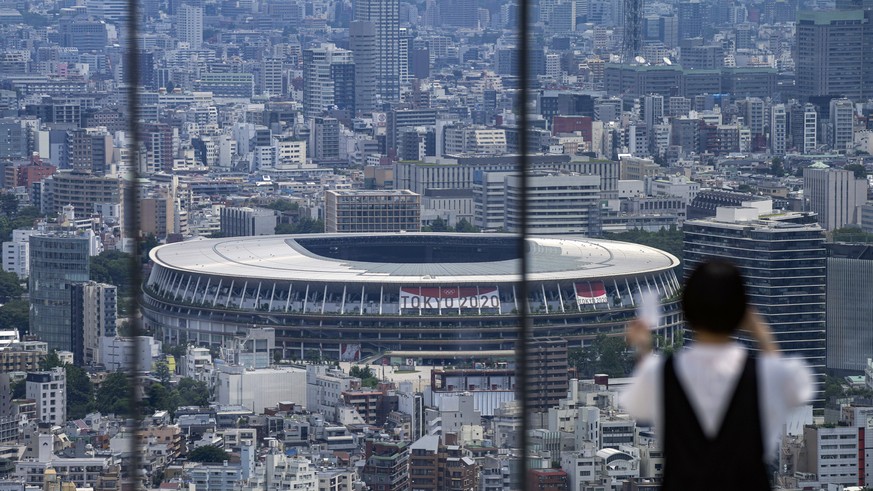 A person wearing a protective mask takes a picture from an observation deck as National Stadium, where the opening ceremony of the Tokyo 2020 Olympics will be held in less than two weeks is seen in th ...