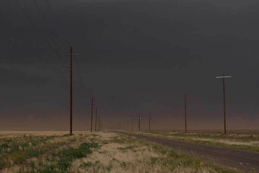 A road lined with poles cuts through the landscape as red dust is kicked up from the ground by a developing storm that darkens the sky during a Project ICECHIP operation with the Red Team, Thursday, J ...