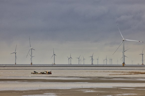 epa09470085 A boat sails past wind turbines in Rudong, Jiangsu province, China, 15 September 2021. The home base is where wind turbines and other offshore equipment are manufactured, maintained, and s ...