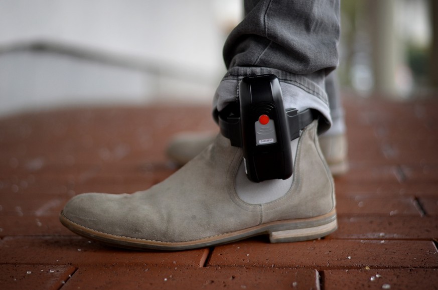 ARCHIV - Ein Mitarbeiter der IT-Stelle der hessischen Justiz veranschaulicht am 11.01.2017 in Bad Vilbel (Hessen), wie eine elektronische Fußfessel getragen wird. Aus Sicherheitsgründen zieht die Zent ...
