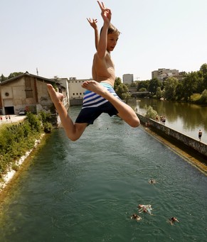 A boy jumps during hot temperatures from a bridge into the Limmat river in Zurich July 3, 2015. On the right is the Sihl river and the headquarters of Swiss retailer Migros. REUTERS/Arnd Wiegmann