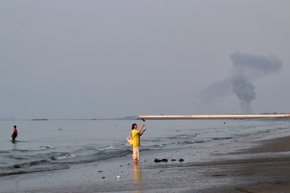KEYPIX - A woman stands at the water's edge along the Strait of Hormuz as a plume of smoke rises in the background following an explosion, off Bandar Abbas, Iran, Monday, July 13, 2026. (KEYSTONE ...