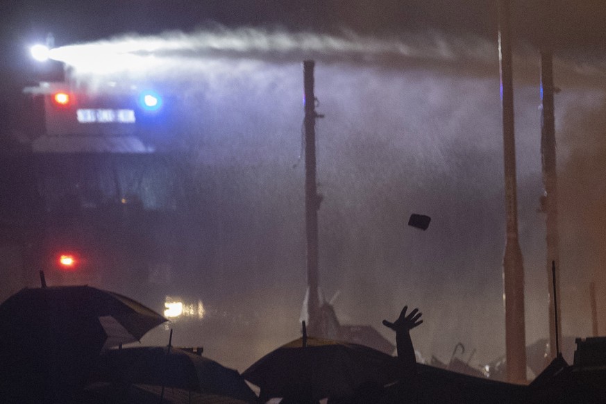 A hand throws a rock as protesters battle water canon and riot police firing tear gas outside the Hong Kong Polytechnic University in Hong Kong on Monday, Nov. 18, 2019. Fiery explosions were seen ear ...