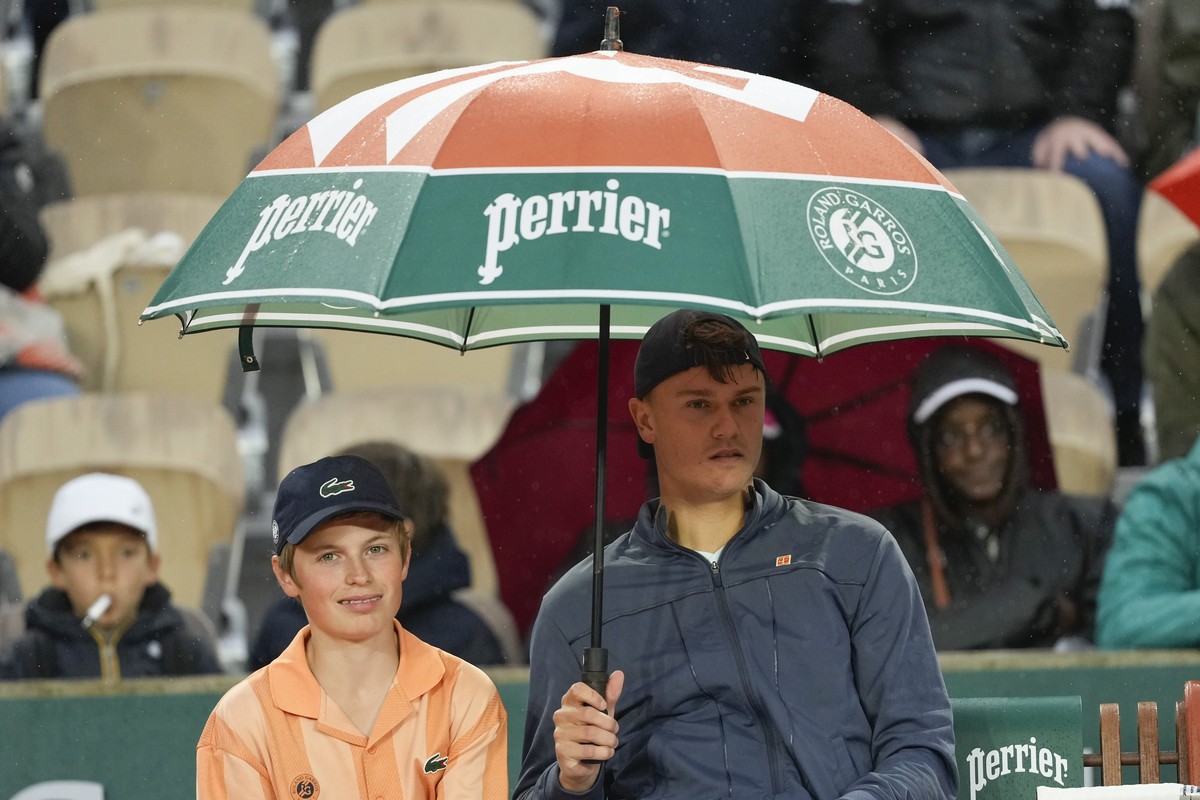 Denmark's Holger Rune holds an umbrella for a ball kid as rain interrupted his third round match of the French Open tennis tournament against Slovakia's Jozef Kovalik at the Roland Garros st ...