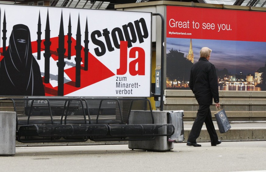 Ein Passant geht an einem Plakat vorbei, welches ein Minarettverbot in der Schweiz fordert, waehrend ein anderes, im Hintergrund, Touristen in der Schweiz willkommen heisst, am Montag, 26. Oktober 200 ...