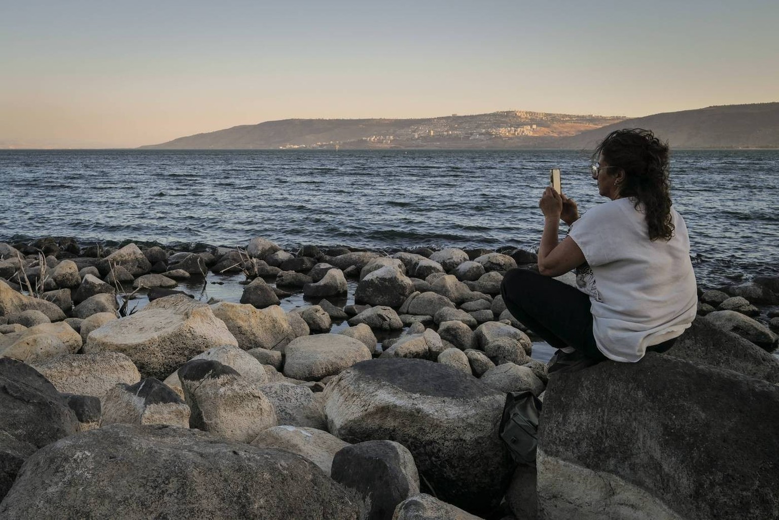 Israel Galilee Sea Shore June 29 A woman takes photo with her phone at the beach of Sea of Galilee and a view of Golan Heights from the Hidden waterfall Ein Ayob near the Christian Pilgrim site of Kfa ...
