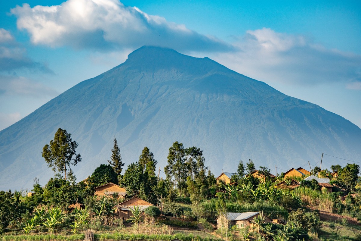 Houses in a small village are dwarfed by the looming presence of a volcanic mountain, Rwanda,