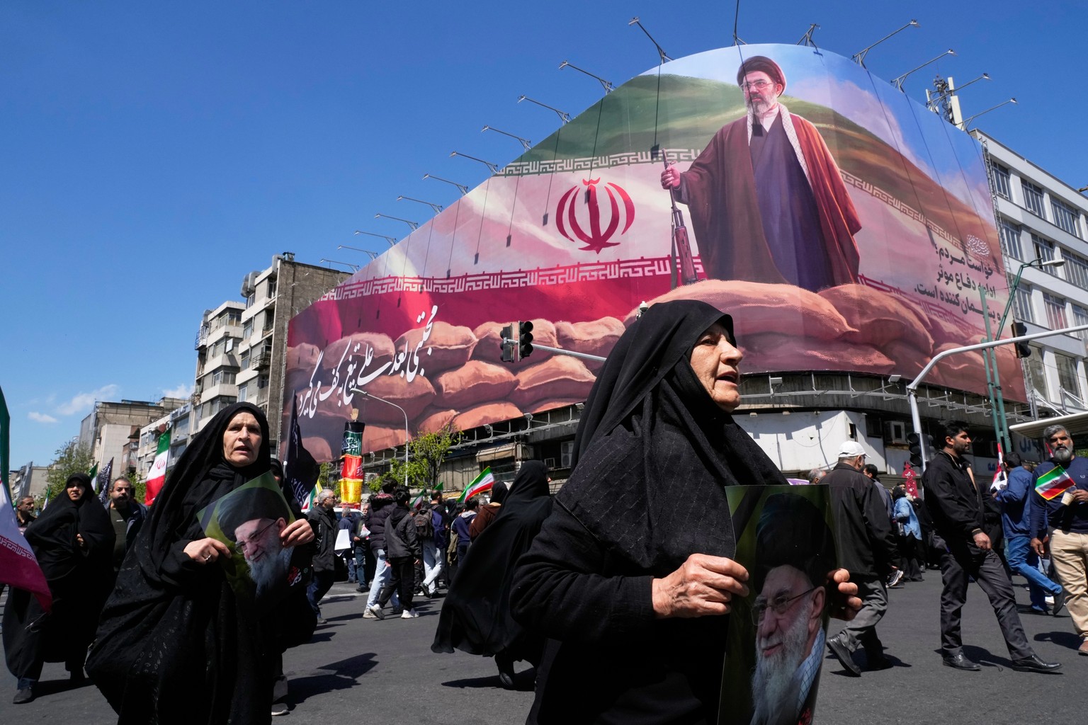 Women walk past a billboard depicting Iran's Supreme Leader Mojtaba Khamenei as government supporters gather to mark the 40th day since the killing of his father, slain Supreme Leader Ayatollah A ...