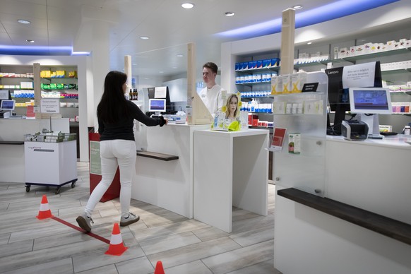 [Gestellte Szene] Eine Plexiglasscheibe trennt eine Kundin vom Apothekenpersonal in der TopPharm Apotheke Kirchberg, am Montag, 30. Maerz 2020 in Kirchberg. (KEYSTONE/Peter Klaunzer)