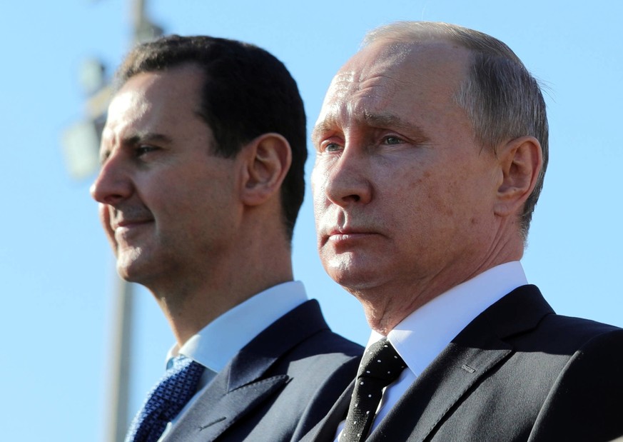 FILE - This Dec. 11, 2017 file photo, shows Russian President Vladimir Putin, right, and Syrian President Bashar Assad watching troops march at the Hemeimeem air base in Syria. In comments published o ...