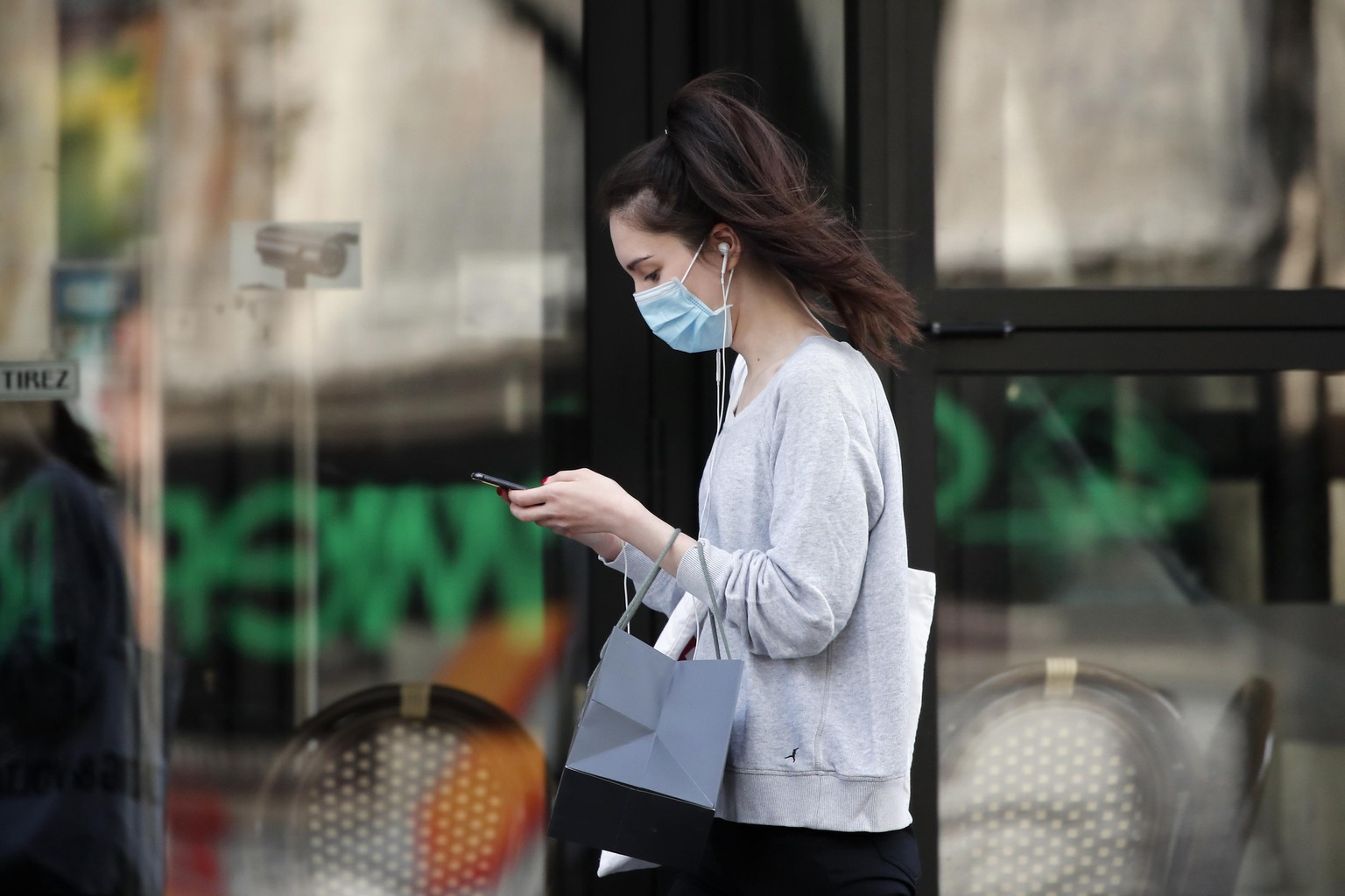 FILE - In this photo taken on April 20, 2020, a woman wearing protective face mask looks at her phone past a closed restaurant during a nationwide confinement to counter the COVID-19, in Paris. French ...