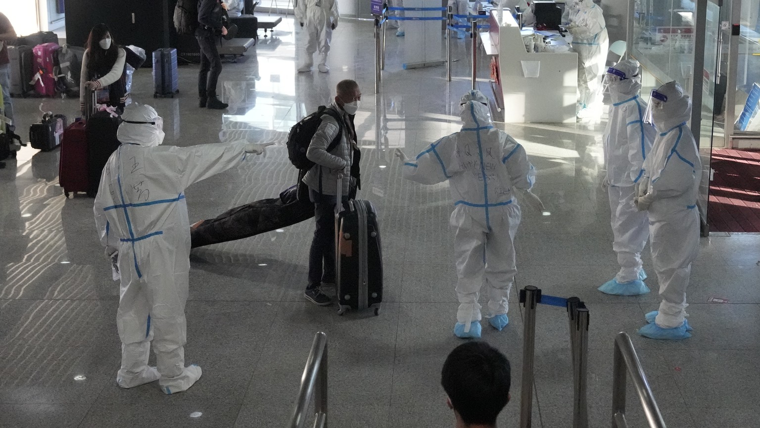 Workers wearing protective suits at the airport assist guests ahead of the 2022 Winter Olympics, Feb. 1, 2022, in Beijing. (AP Photo/Aaron Favila)