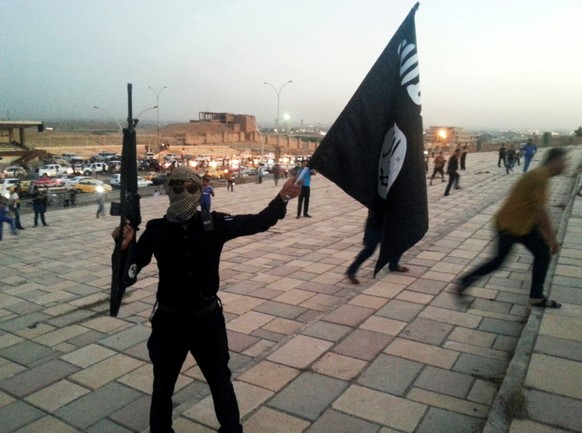 A fighter of the Islamic State of Iraq and the Levant (ISIL) holds an ISIL flag and a weapon on a street in the city of Mosul, Iraq June 23, 2014. REUTERS/Stringer/File Photo