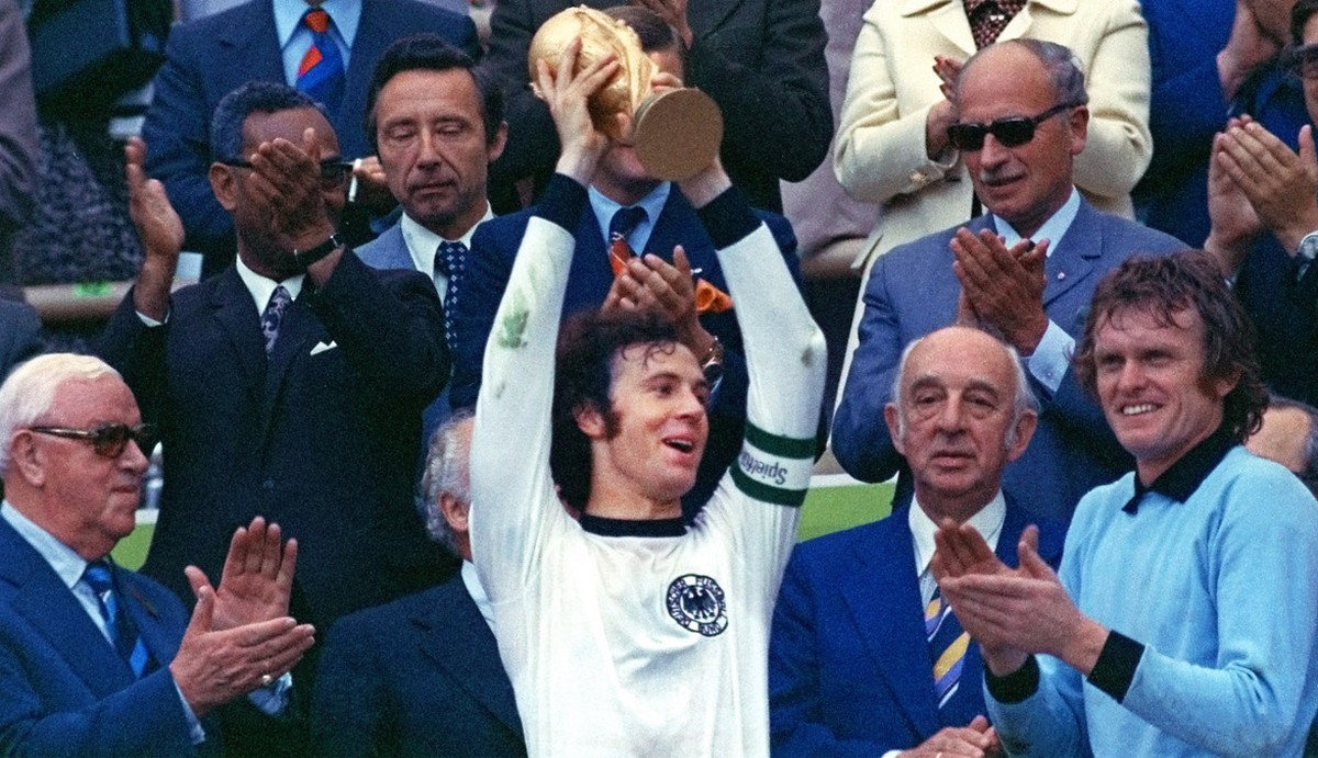 Surrounded by applauding spectators, Franz Beckenbauer, center, team captain of the winning German national soccer team at the 1974 world soccer championship presents the trophy in Munich's, Germ ...